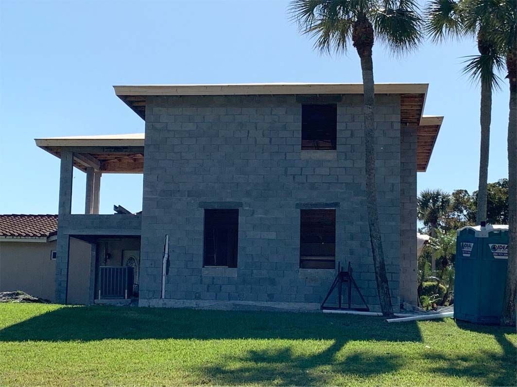 A brick house is being built in the middle of a lush green field.