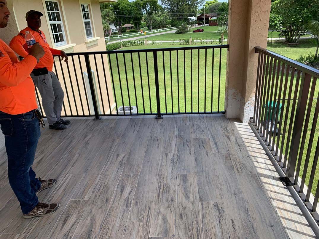Two men are standing on a balcony looking out over a lush green field.