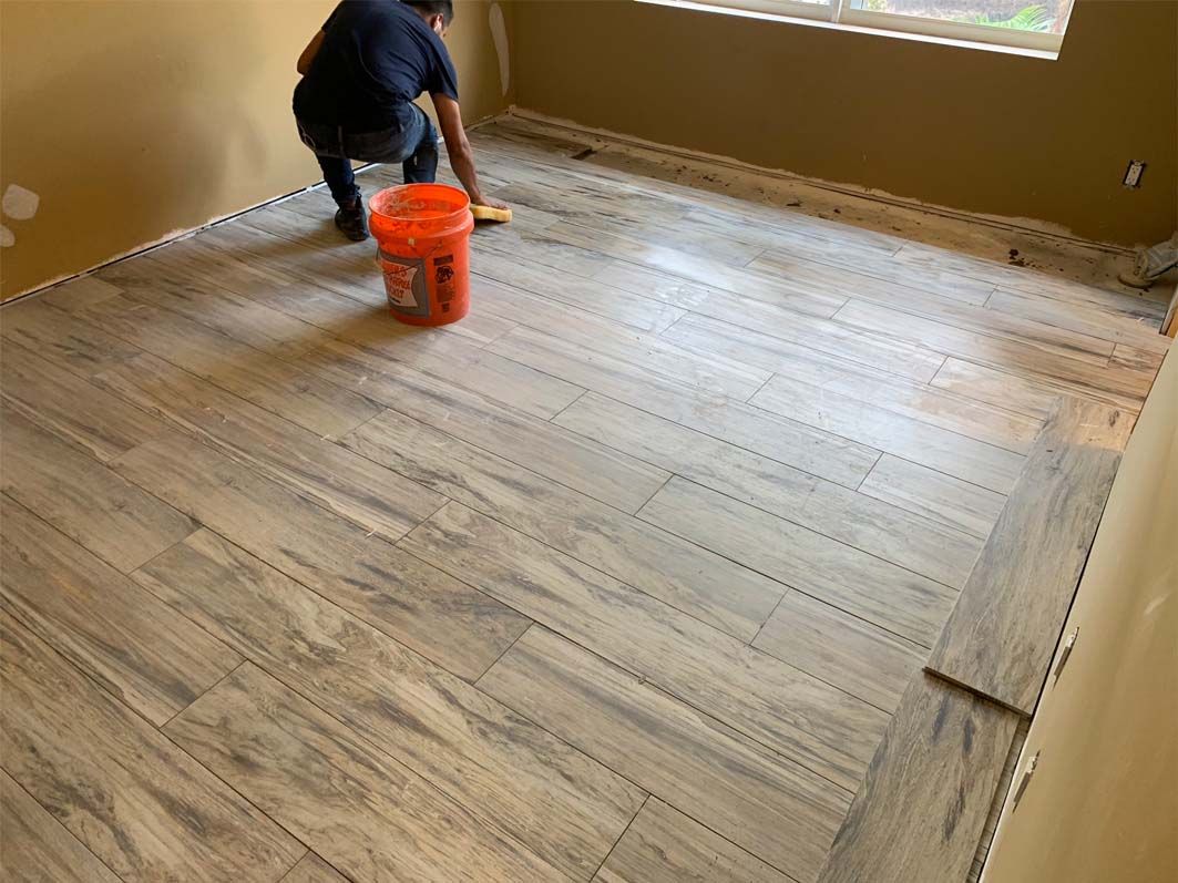A man is cleaning a wooden floor with an orange bucket.