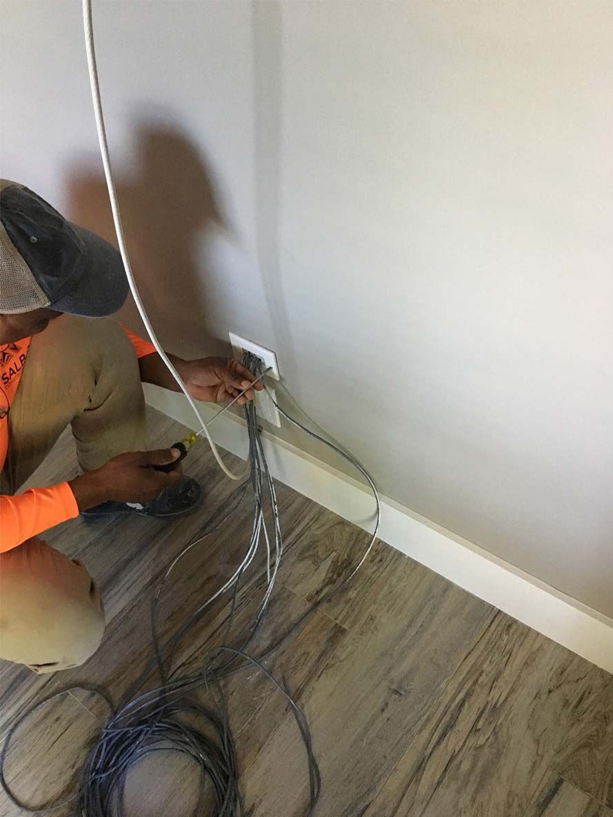 A man is kneeling on the floor working on a wall.