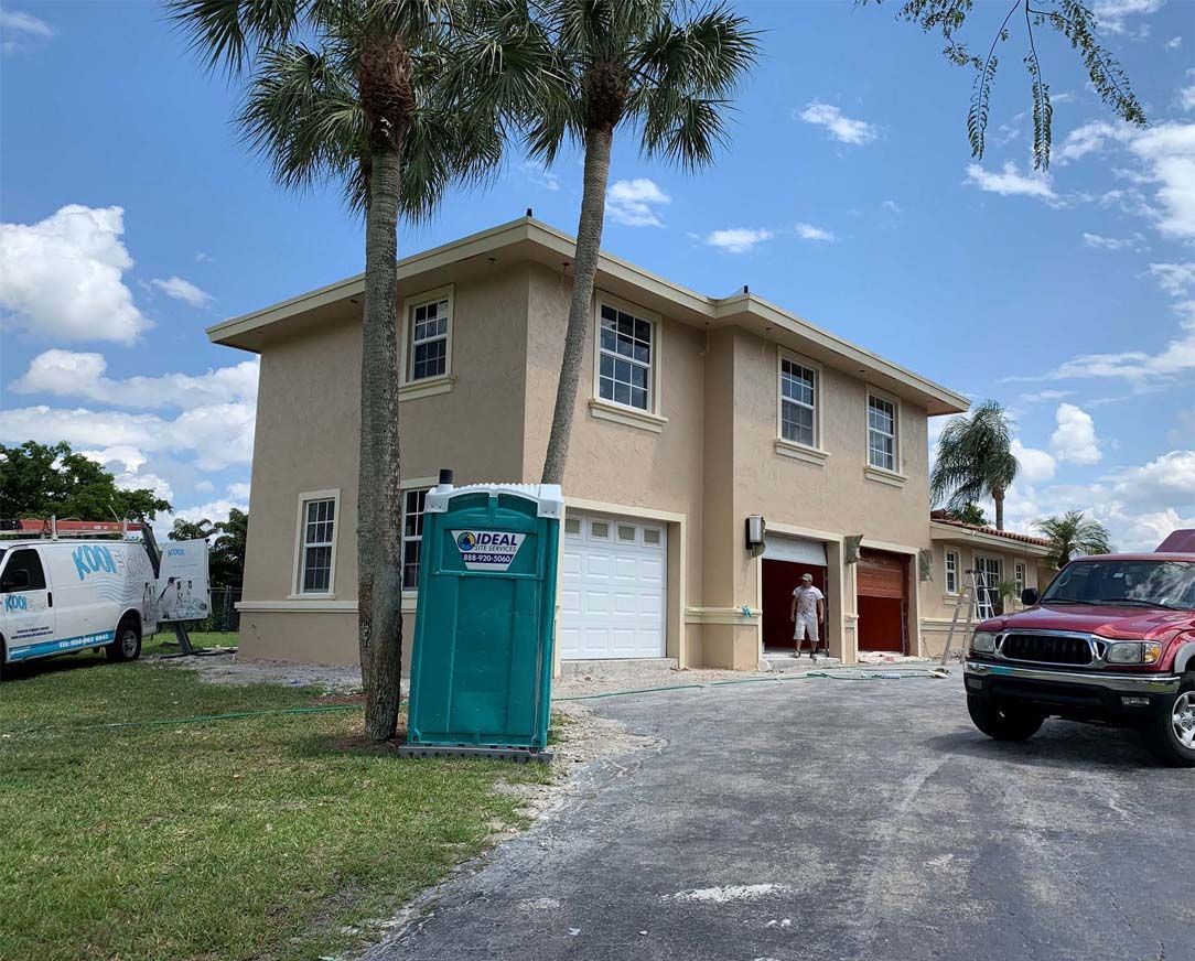 A green portable toilet is parked in front of a house.