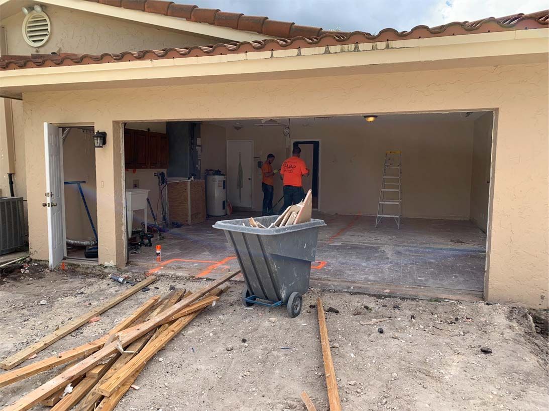 A man is standing in a garage with a wheelbarrow full of wood.