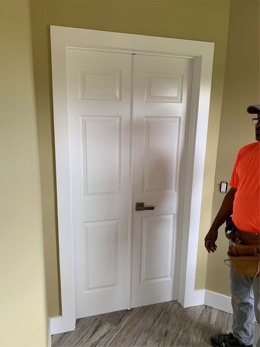 A man in an orange shirt is standing in front of a white door.