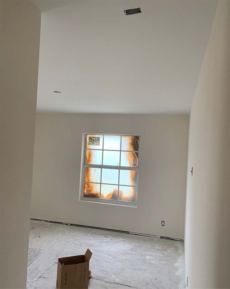 An empty room with a window and a cardboard box on the floor.