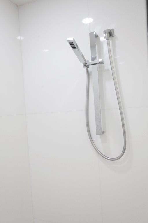 A shower head is hanging on a white wall in a bathroom.