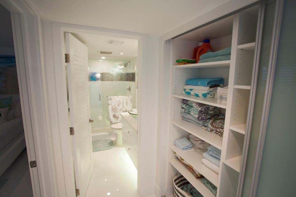 A bathroom with a walk in closet filled with clothes and towels.