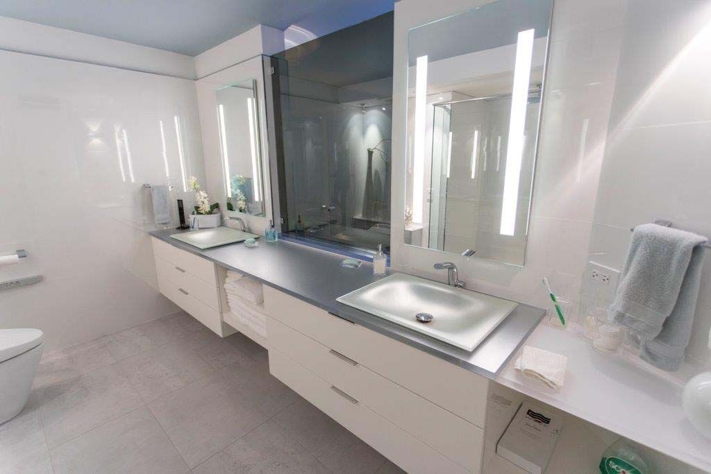 A bathroom with two sinks , two mirrors and a toilet.