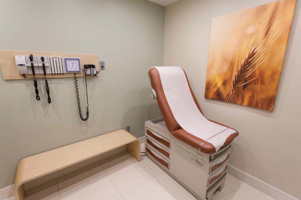 A doctor 's office with a brown exam table and a painting on the wall.