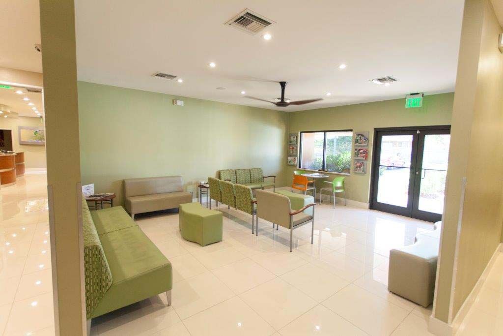 A large waiting room with green chairs and a ceiling fan.