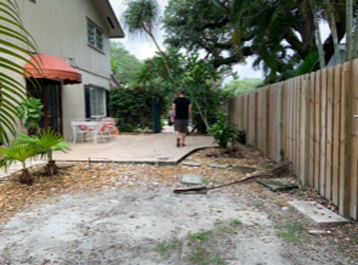 A man is standing in a backyard next to a wooden fence.
