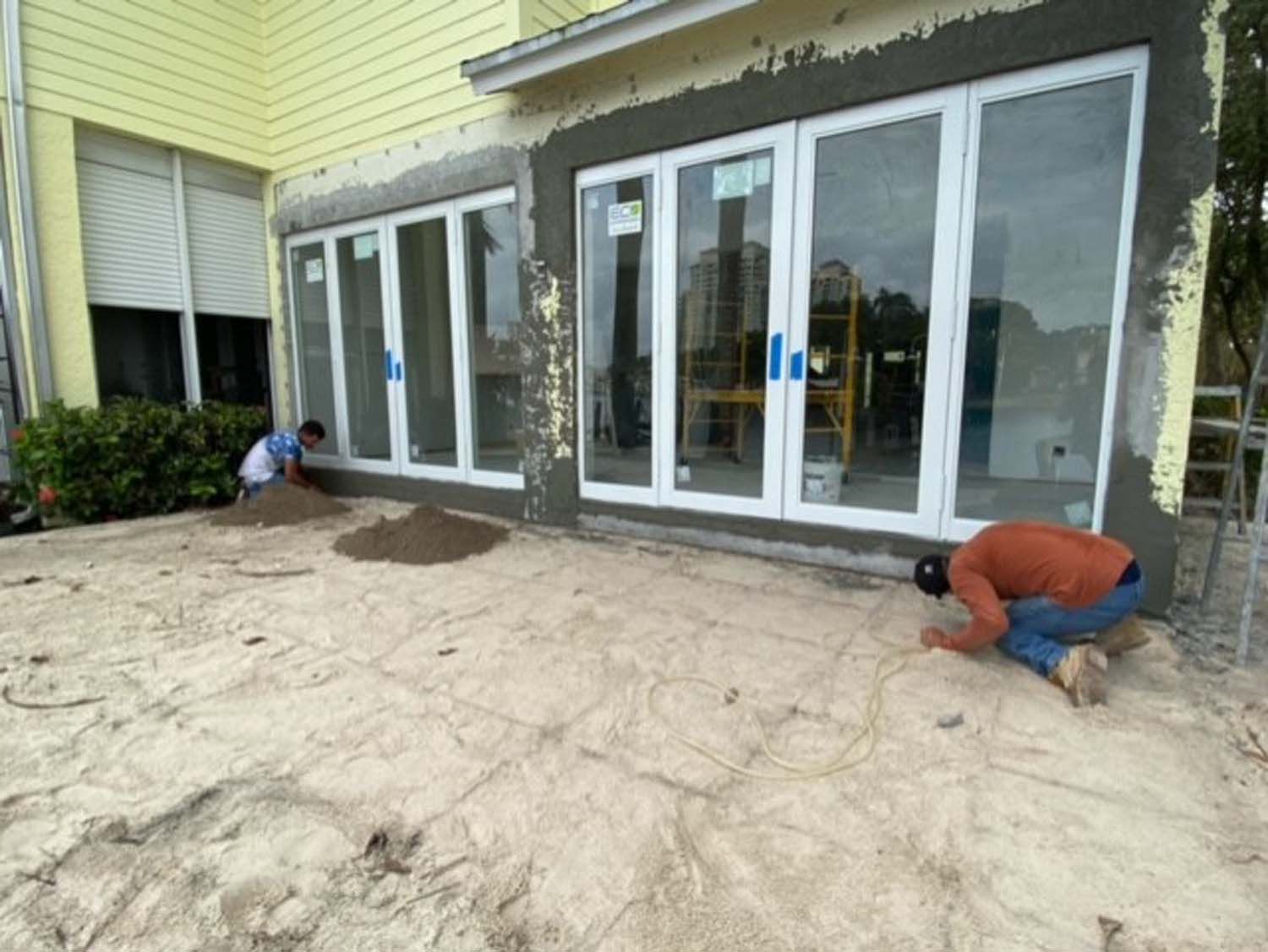 Two men are working on a patio in front of a house.