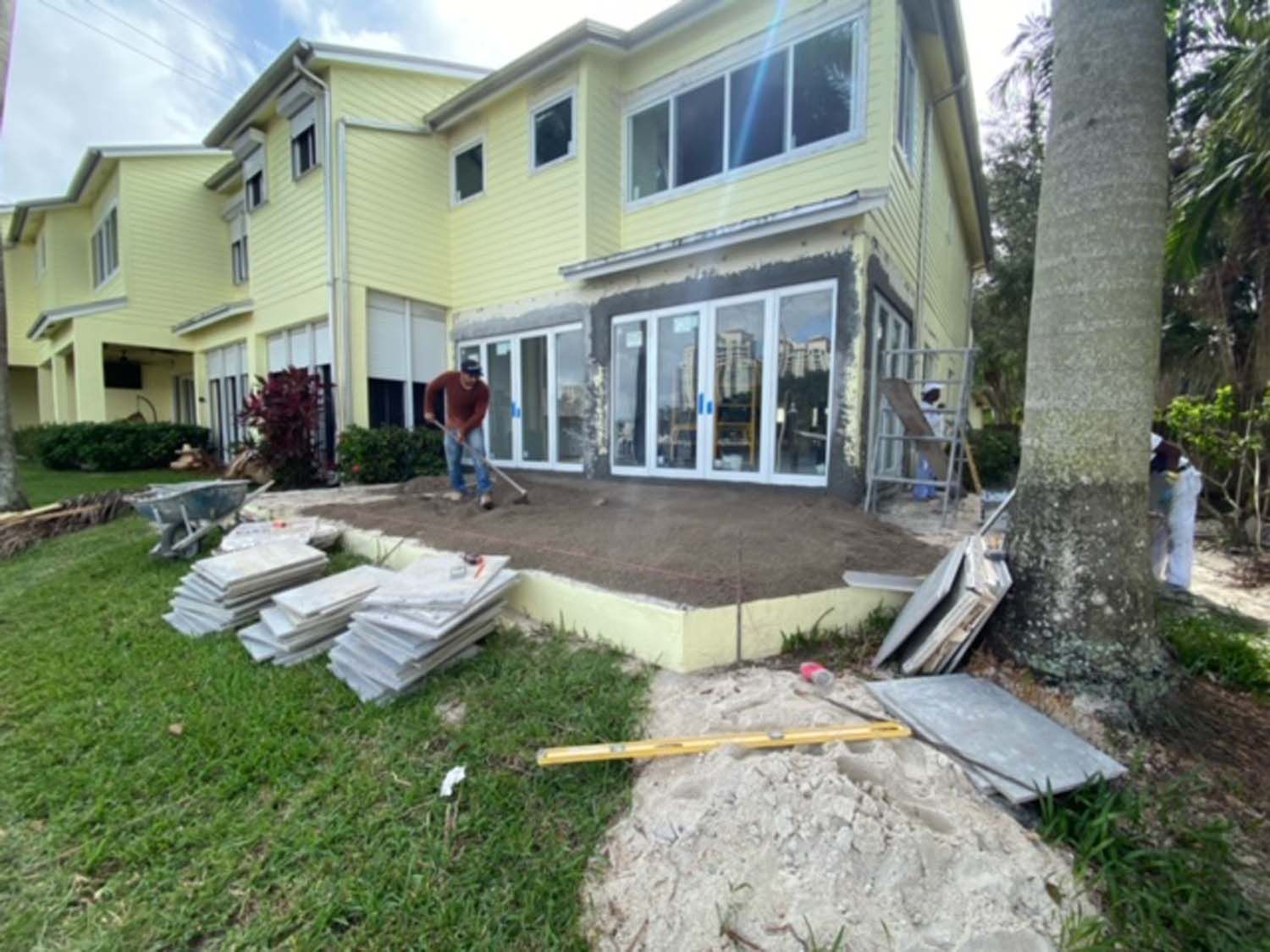 A large yellow house with a patio being built in front of it.