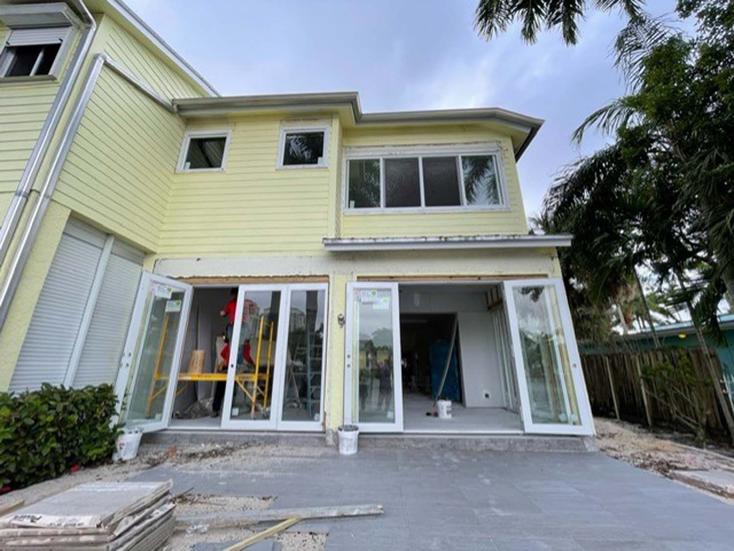 A yellow house with sliding glass doors is under construction.