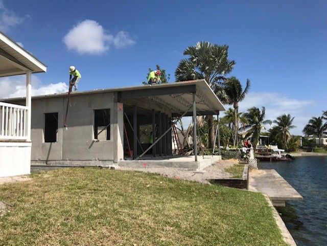 Two men are working on the roof of a house next to a body of water.