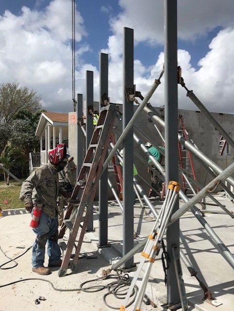 A man wearing a welding helmet is standing next to a ladder on a construction site.