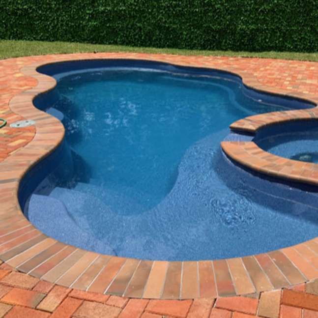 A large swimming pool surrounded by bricks and a hot tub