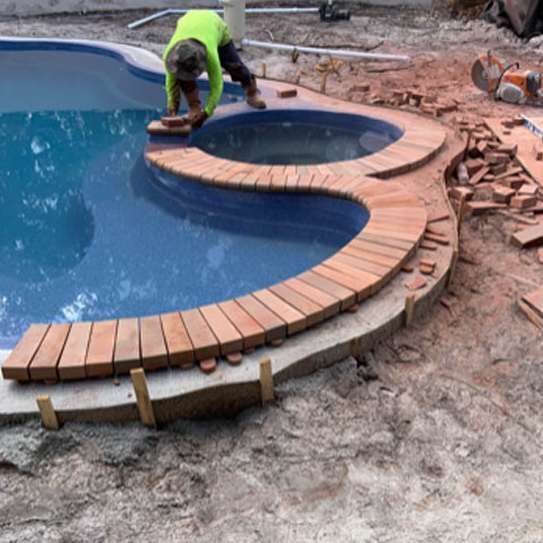 A man is working on a wooden walkway around a swimming pool.