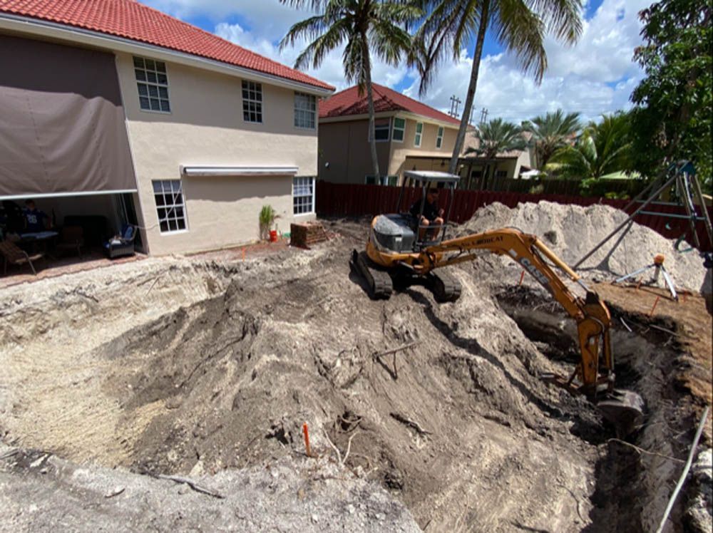 An excavator is digging a hole in the ground in front of a house.