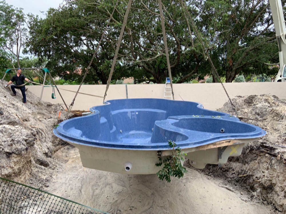 A blue swimming pool is being lifted into the ground by a crane.