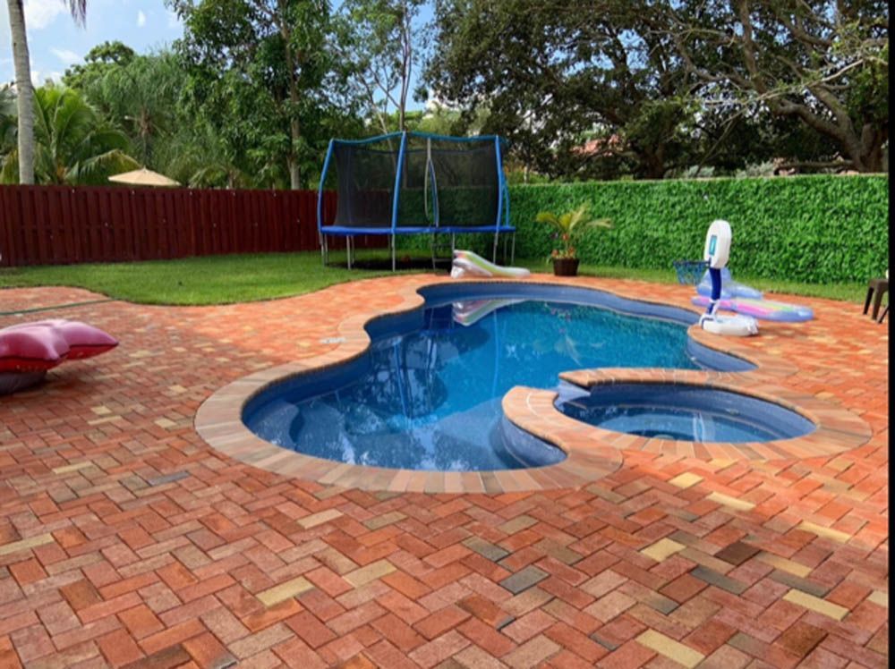 A large swimming pool with a trampoline in the backyard.