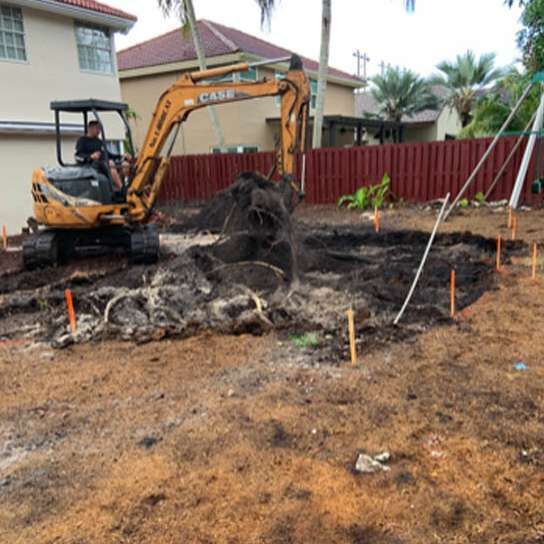An excavator is digging a hole in the dirt in front of a house.