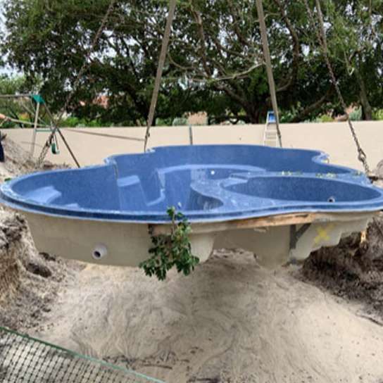 A blue swimming pool is being lifted into the ground by a crane.