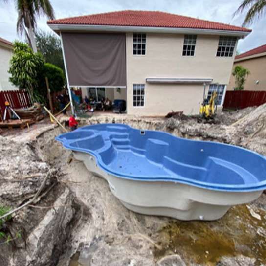 A large blue and white swimming pool is being built in front of a house.