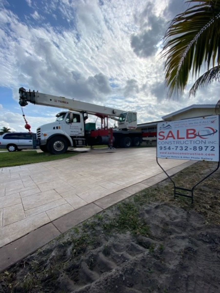 A truck with a crane on it is parked in a driveway next to a palm tree.