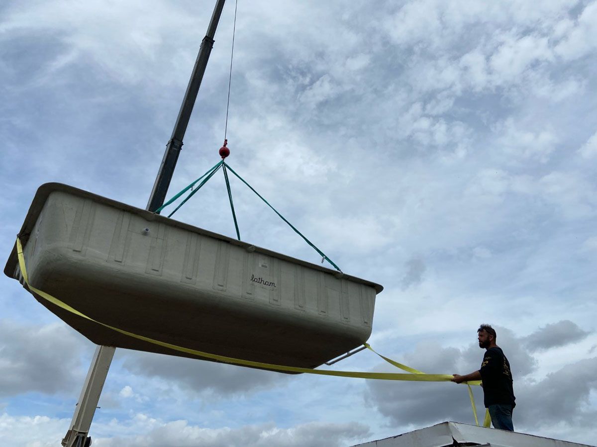 A man is standing on top of a building while a crane lifts a bathtub into the air.