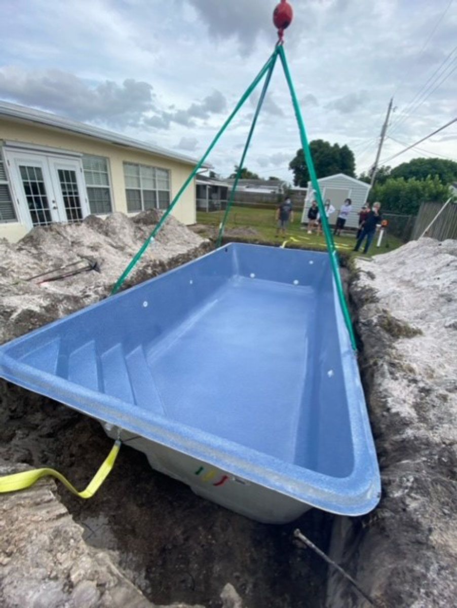 A blue swimming pool is being lifted out of the ground by a crane.