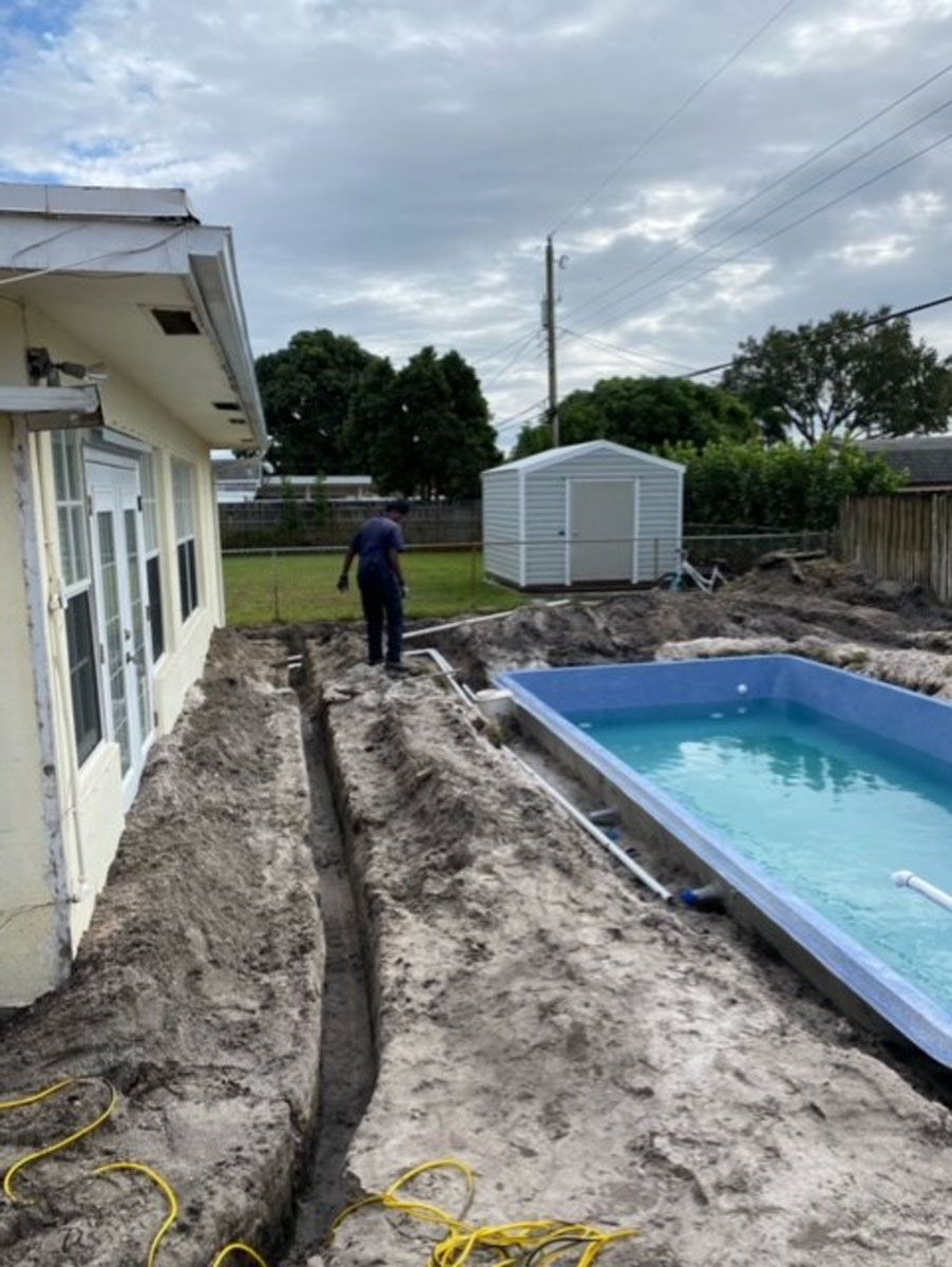 A man is standing in the dirt next to a swimming pool.