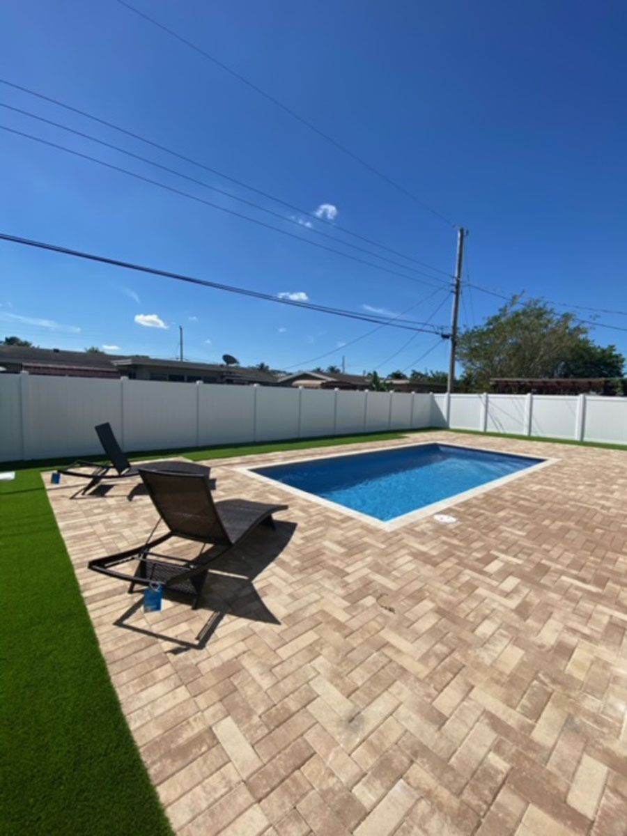 A large swimming pool is surrounded by a brick patio and chairs.
