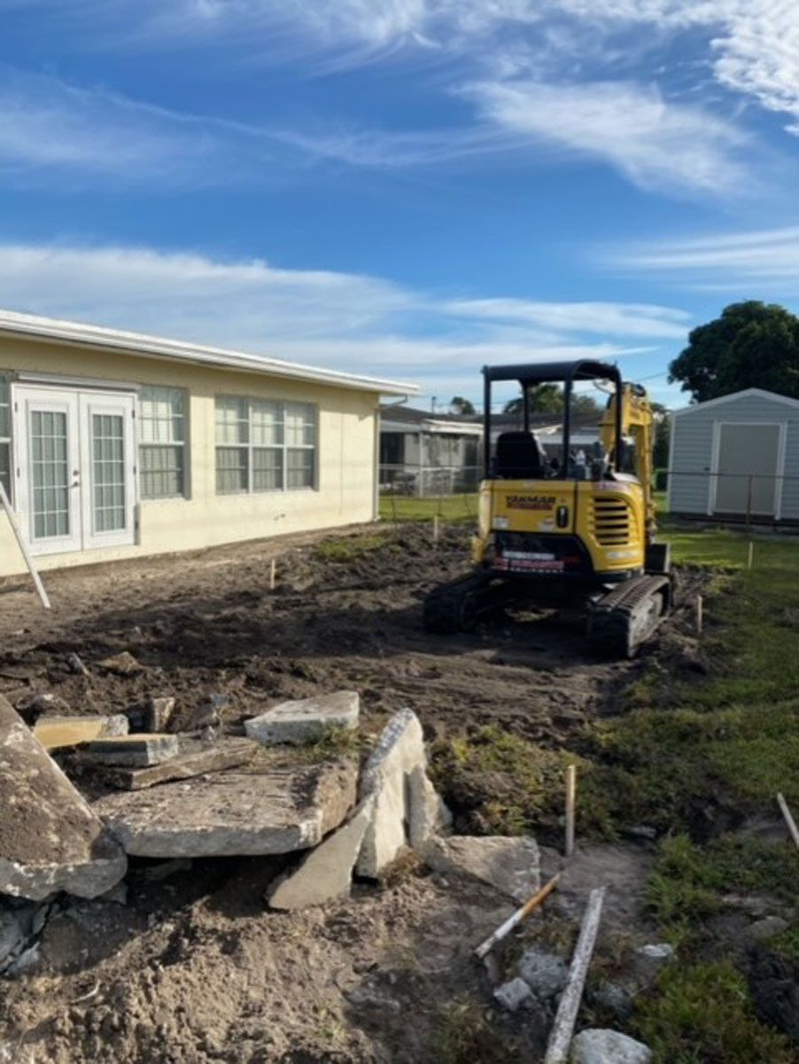 A yellow excavator is sitting in the dirt in front of a house.