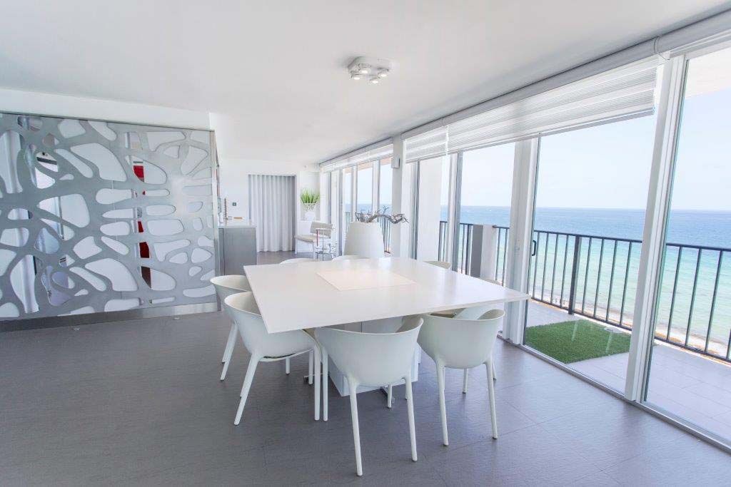 A dining room with a table and chairs and a balcony overlooking the ocean