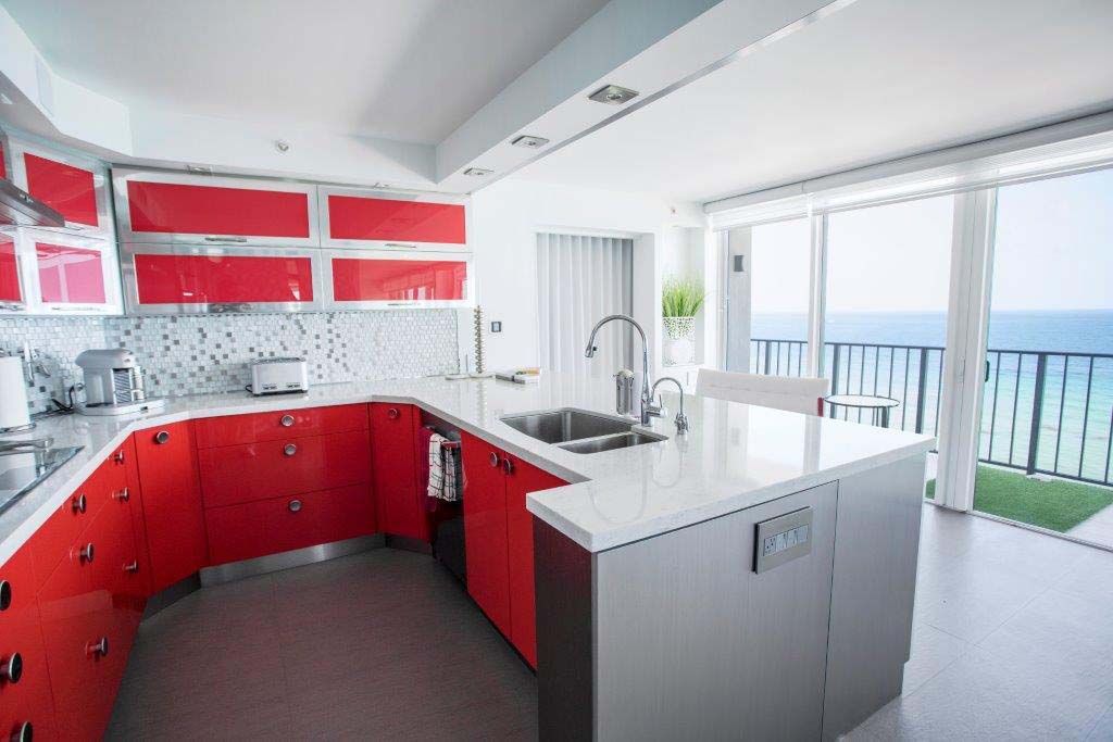 A kitchen with red cabinets and white counter tops with a view of the ocean.