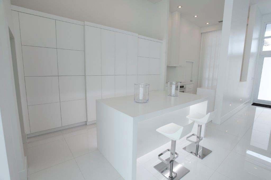 A kitchen with all white cabinets , counter tops , and stools.