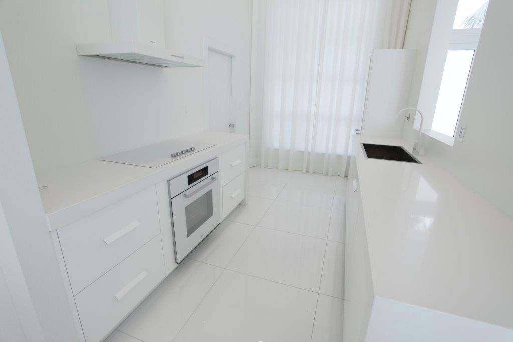 An empty kitchen with white cabinets , a stove , and a sink.