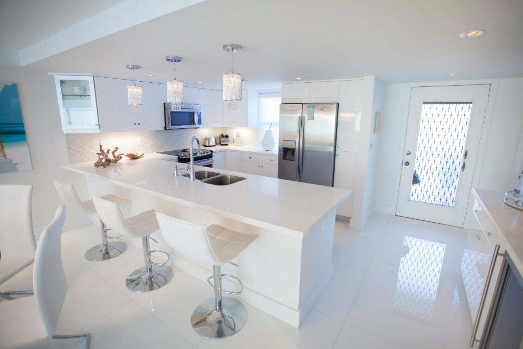 A kitchen with white cabinets , counter tops , stools and a refrigerator.