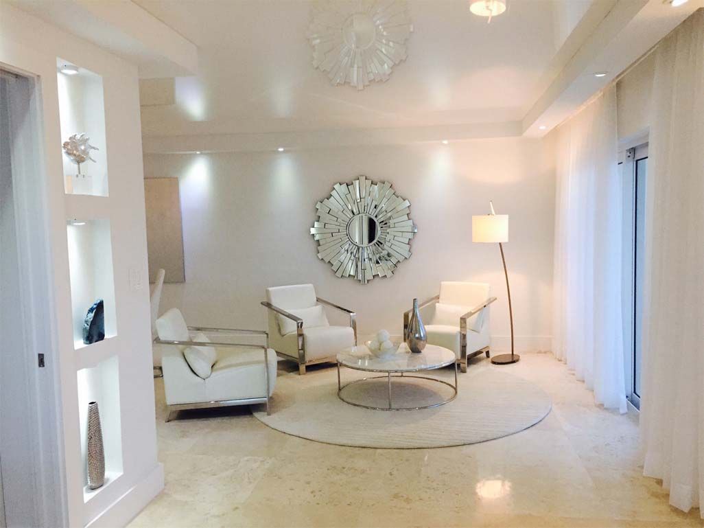 A living room with white furniture and a mirror on the wall