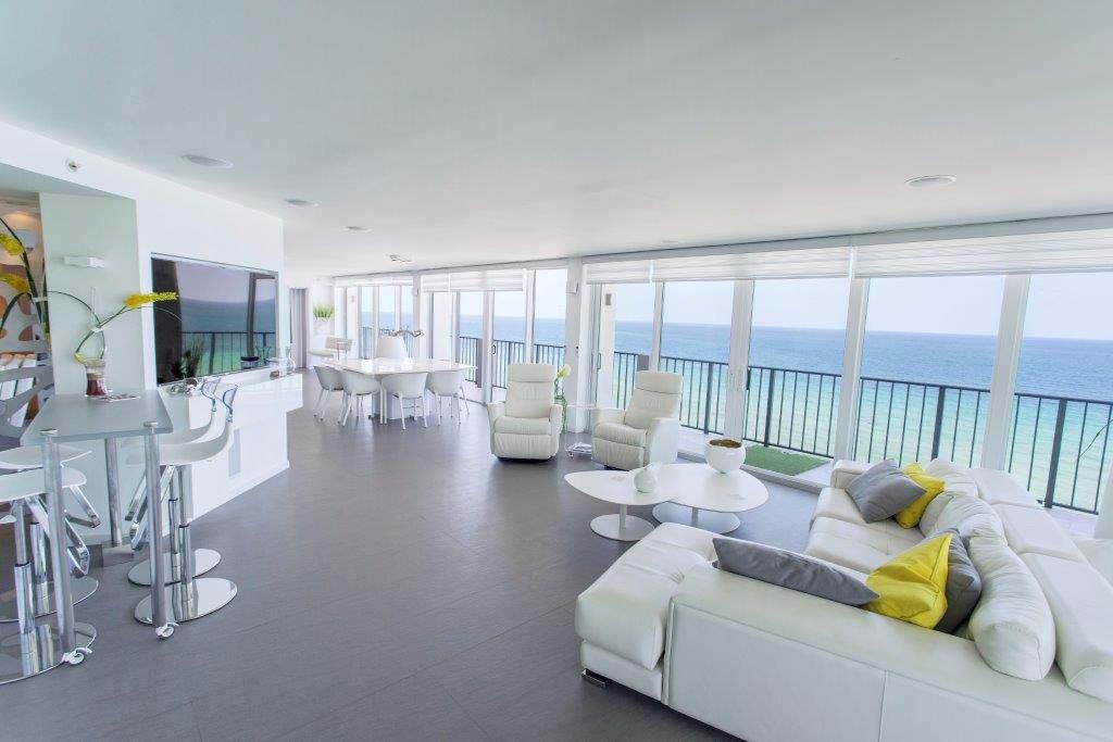 A living room with a couch , chairs , tables and a view of the ocean.