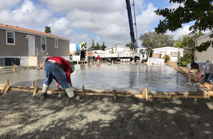A man is working on a concrete driveway in front of a mobile home.