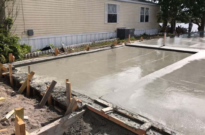 A concrete driveway is being built in front of a mobile home.