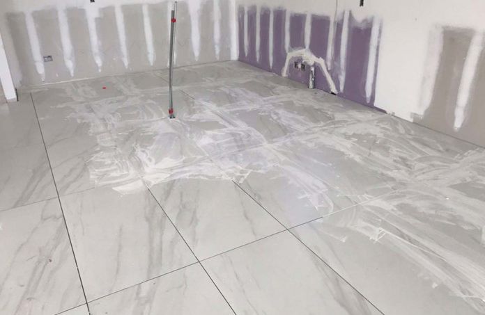 A room with white tiles and a mop on the floor.