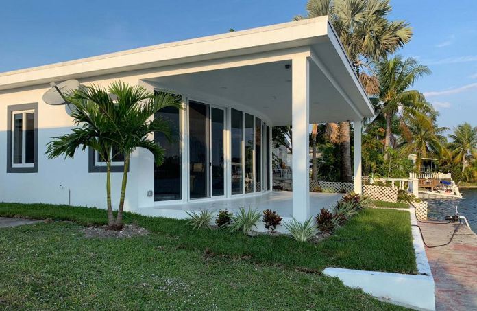 A white house with a porch and a lot of windows is sitting next to a body of water.