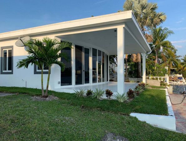 A white house with a porch and palm trees in front of it