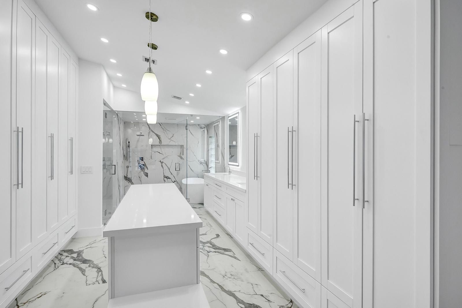 A large walk in closet with white cabinets and marble floors.