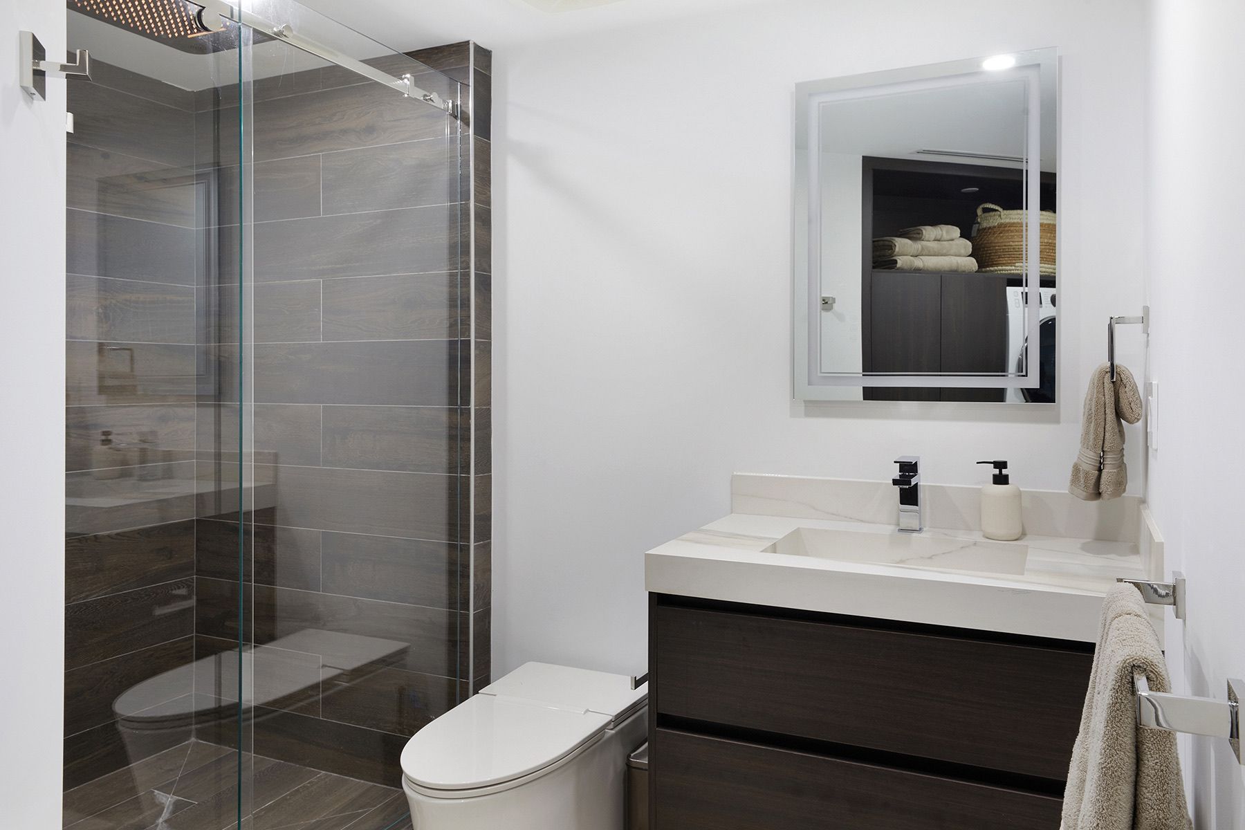 A bathroom with a toilet , sink , mirror and walk in shower.