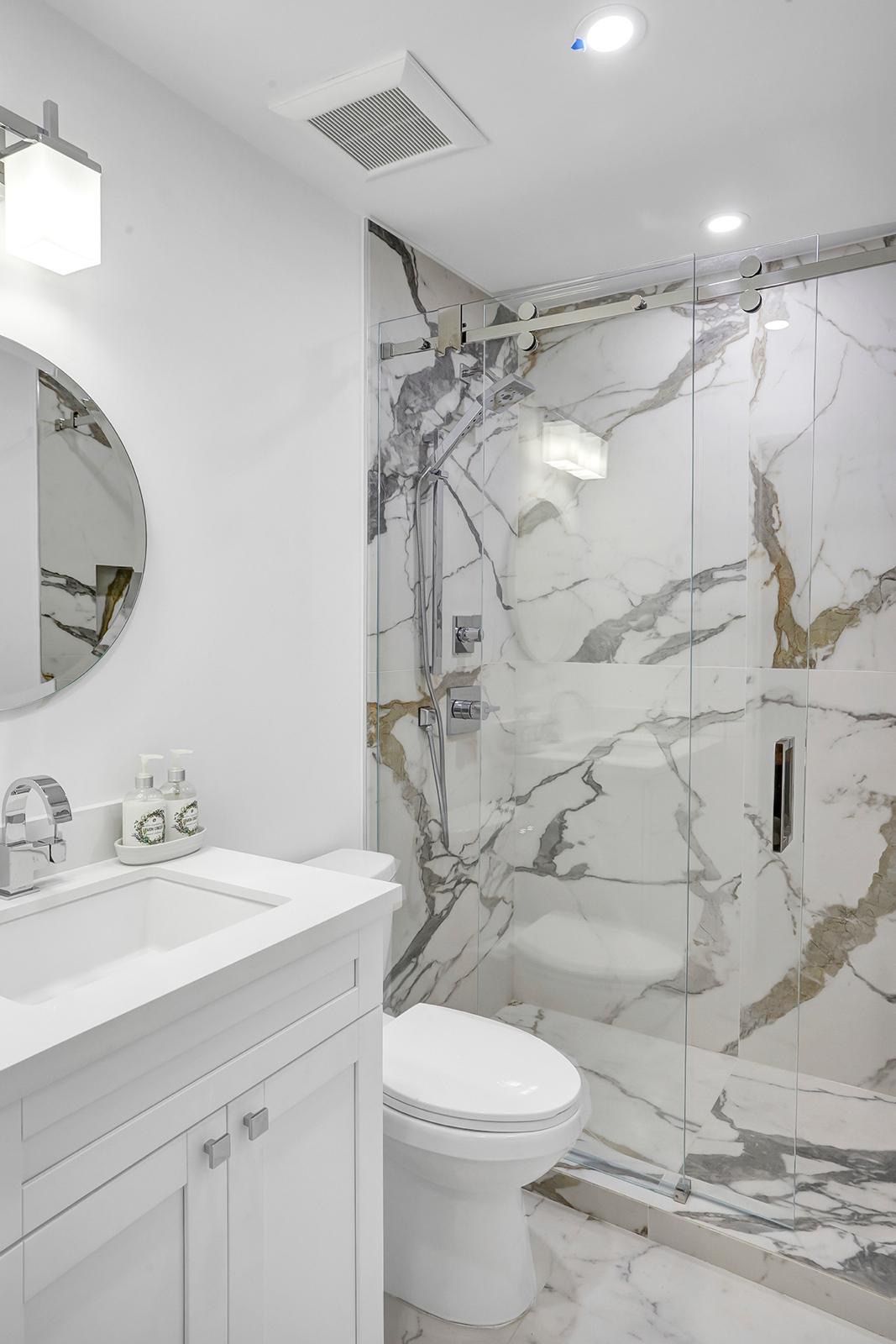 A bathroom with a toilet , sink , mirror and shower.