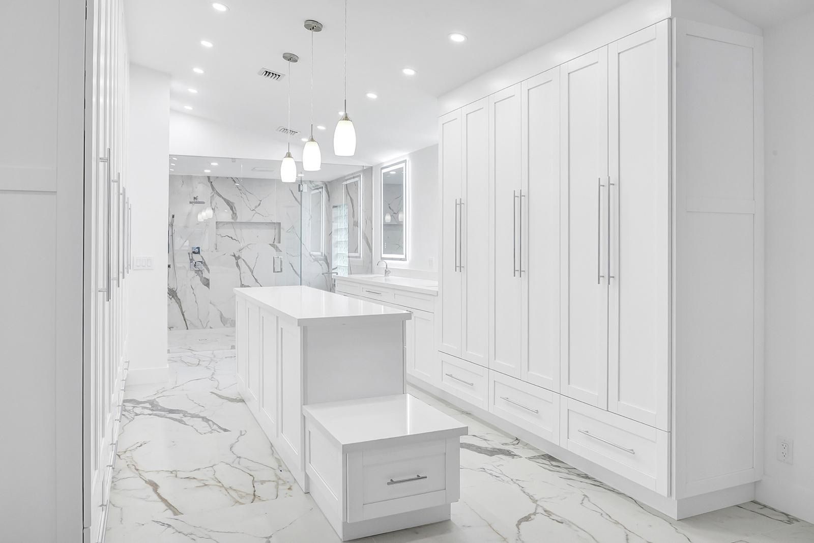 A walk in closet with white cabinets and marble floors.