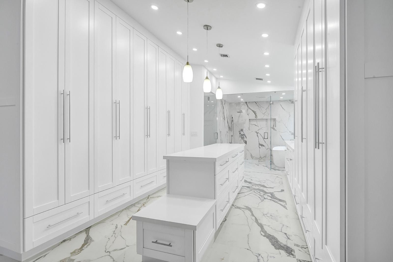 A large walk in closet with white cabinets and marble floors.